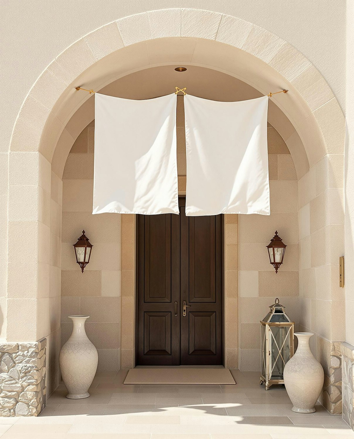 An elegant symmetrical entrance with wooden double doors, white fabric panels, ceramic vases and hanging lanterns set beneath a stone archway