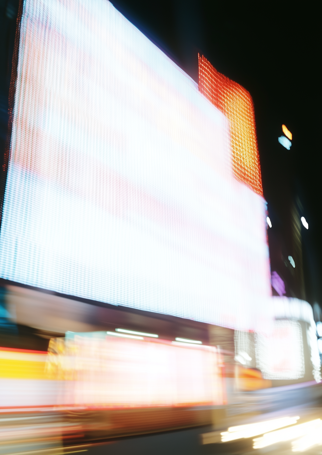 A blurred night cityscape of bright illuminated billboards and streaking light