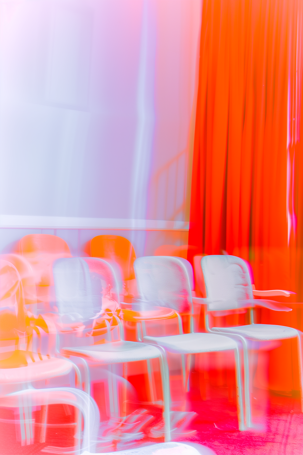 Rows of pale chairs blurred by camera motion in front of a deep red stage curtain