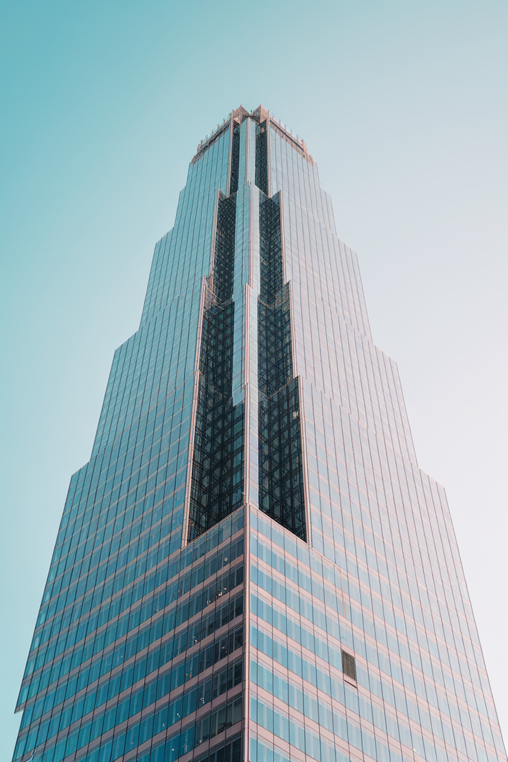 A sleek glass-fronted skyscraper reflecting blue sky, its facade made of strong vertical lines