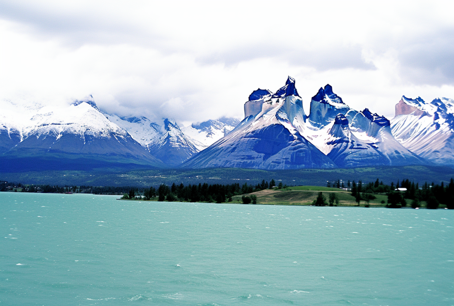 Snow-capped mountains rising steeply above a turquoise lake under a heavy, overcast sky